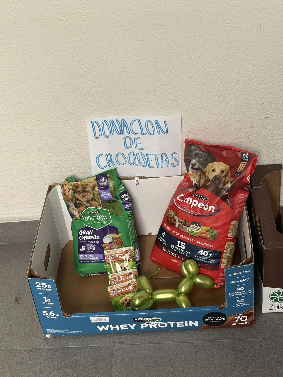 Caja de acopio con un letrero hecho a mano que dice Donación de croquetas, con bolsas de alimento para perro adentro.